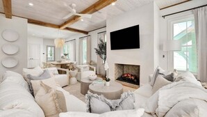 A modern living room with a fireplace, white furniture, and a large TV on the wall.