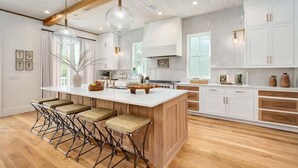 A modern kitchen with a large island, bar stools, white cabinetry, and wooden beams.
