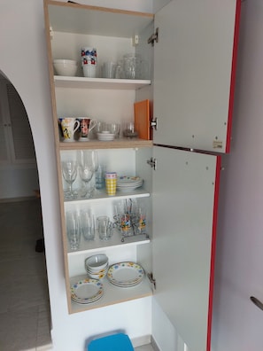 Kitchen area with refrigerator and shelving, stocked with kitchenware.