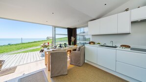 A modern kitchen with a view of the sea, a dining area with a table and chairs, and a small seating area with cushions. - The Billy Shed  - Eype, Bridport (Bridport)