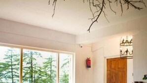 A dining area with a long table set for multiple people, large windows with a view of trees, and a chandelier hanging above. - Seclude Shimla Taraview (Shimla)