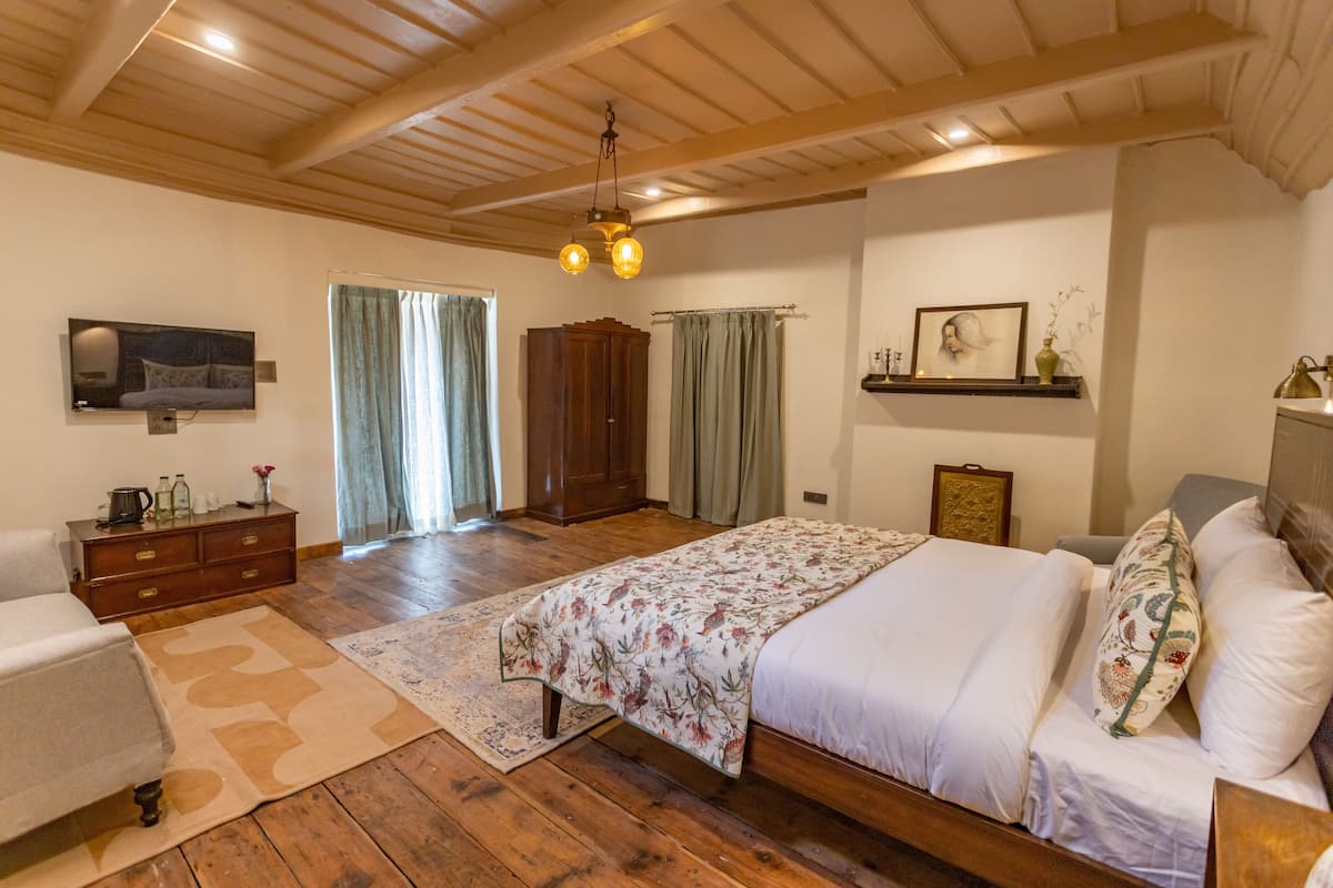 Een slaapkamer met een houten plafond, een bed met bloemenbedrukking, een houten dressoir, een televisie aan de muur en een raam met gordijnen.