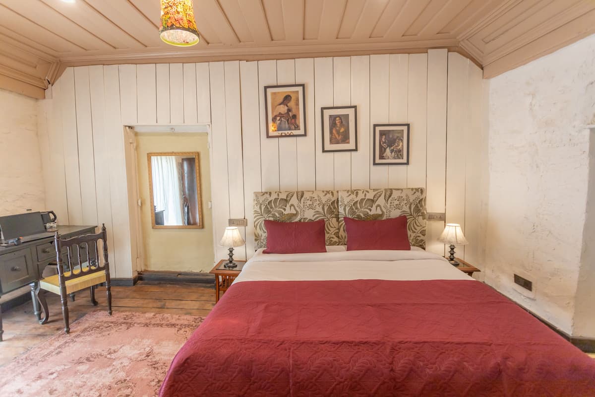 Een slaapkamer met een groot bed, twee nachtkastjes met lampen, een houten bureau en een deur.