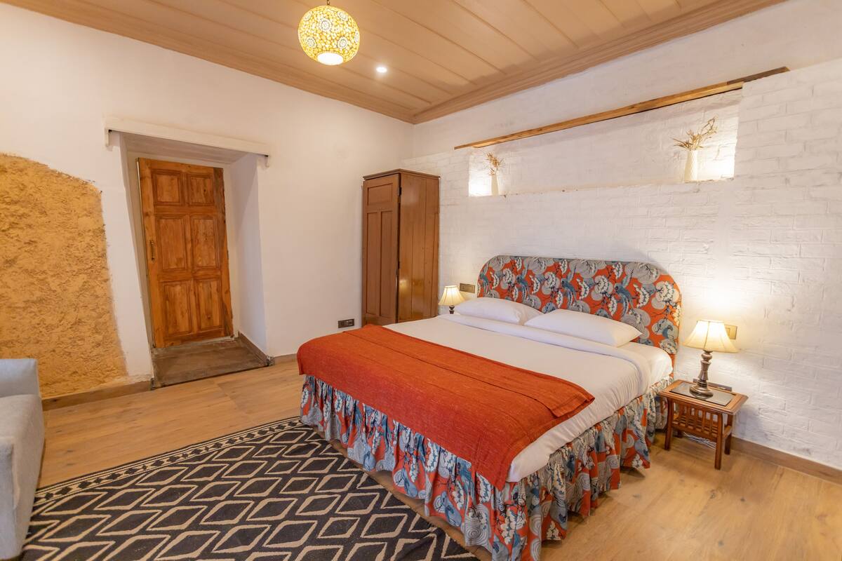 Een slaapkamer met een houten bed, een kamerkleed met een patroon, een witte baksteenmuur en een houten deur.