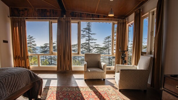 A bedroom with a large window, a bed, a chair, and a dresser. - Seclude Shimla Taraview (Shimla)