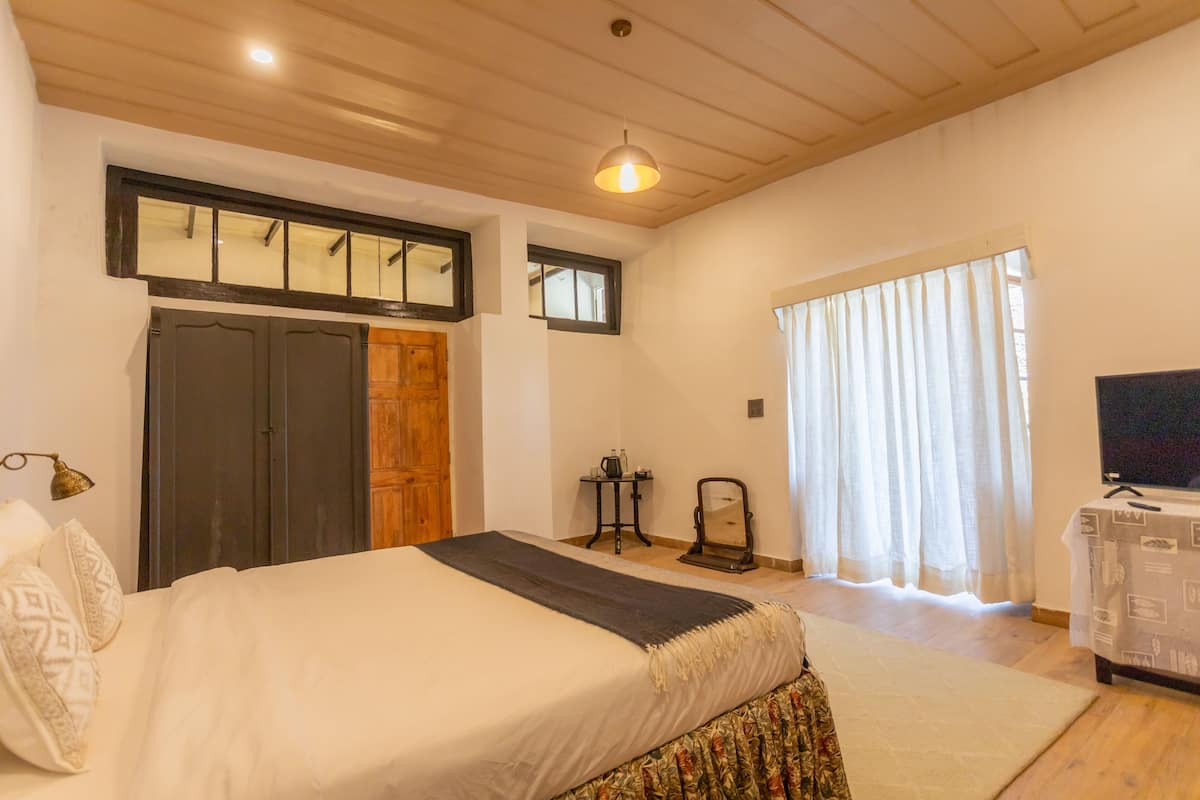 Een slaapkamer met een groot bed, een houten plafond, een televisie en een raam met gordijnen.
