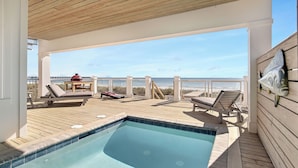 Ett trädäck med en pool, solstolar och utsikt över stranden och havet.