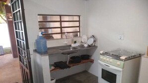 Une cuisine de taille réduite, équipée d’une cuisinière à gaz, d’un évier et d’une fenêtre située au-dessus du plan de travail.