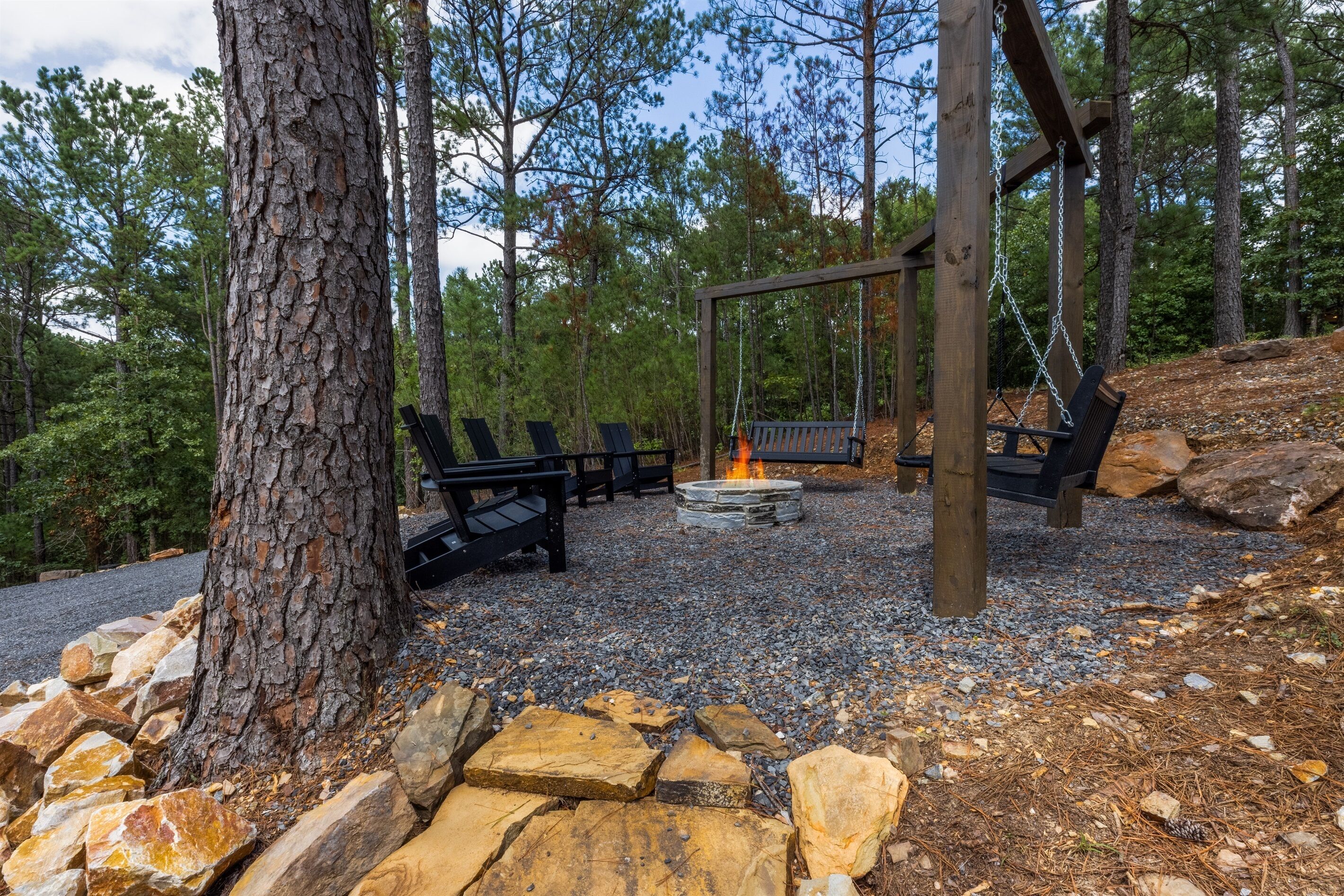 Un ensemble de balançoires en bois, un foyer et plusieurs bancs installés dans une zone boisée.