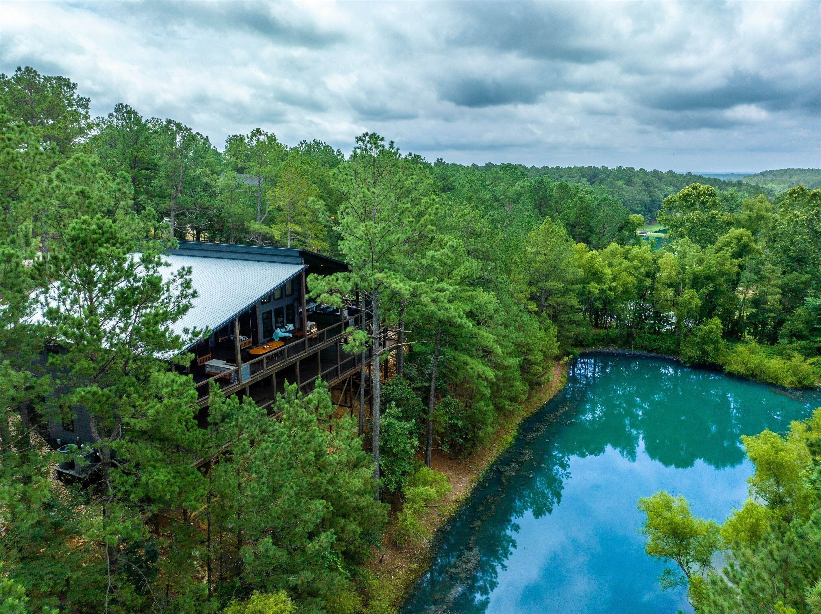 A cabin with a deck overlooking a river, surrounded by dense forest.