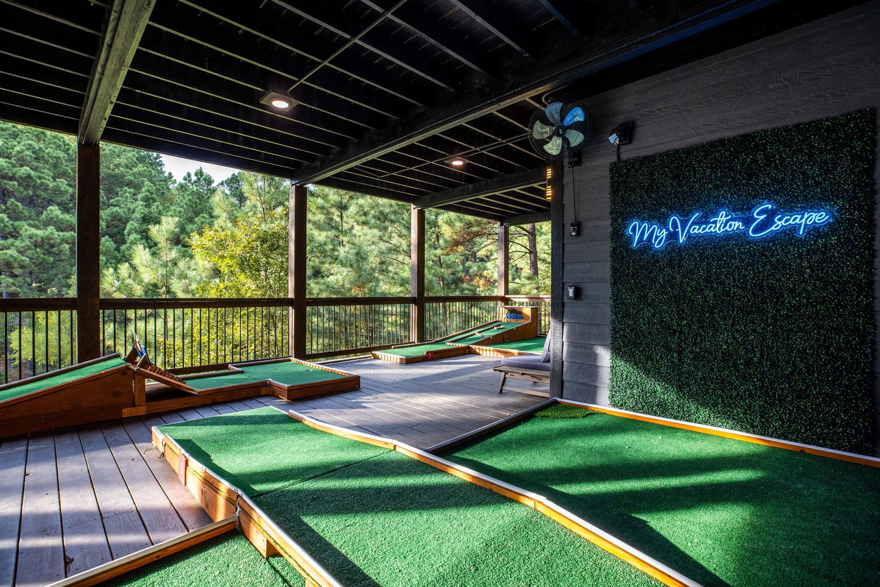 A miniature golf course with a neon sign reading "My Vacation Escape" and a view of a forest through the open roof structure.