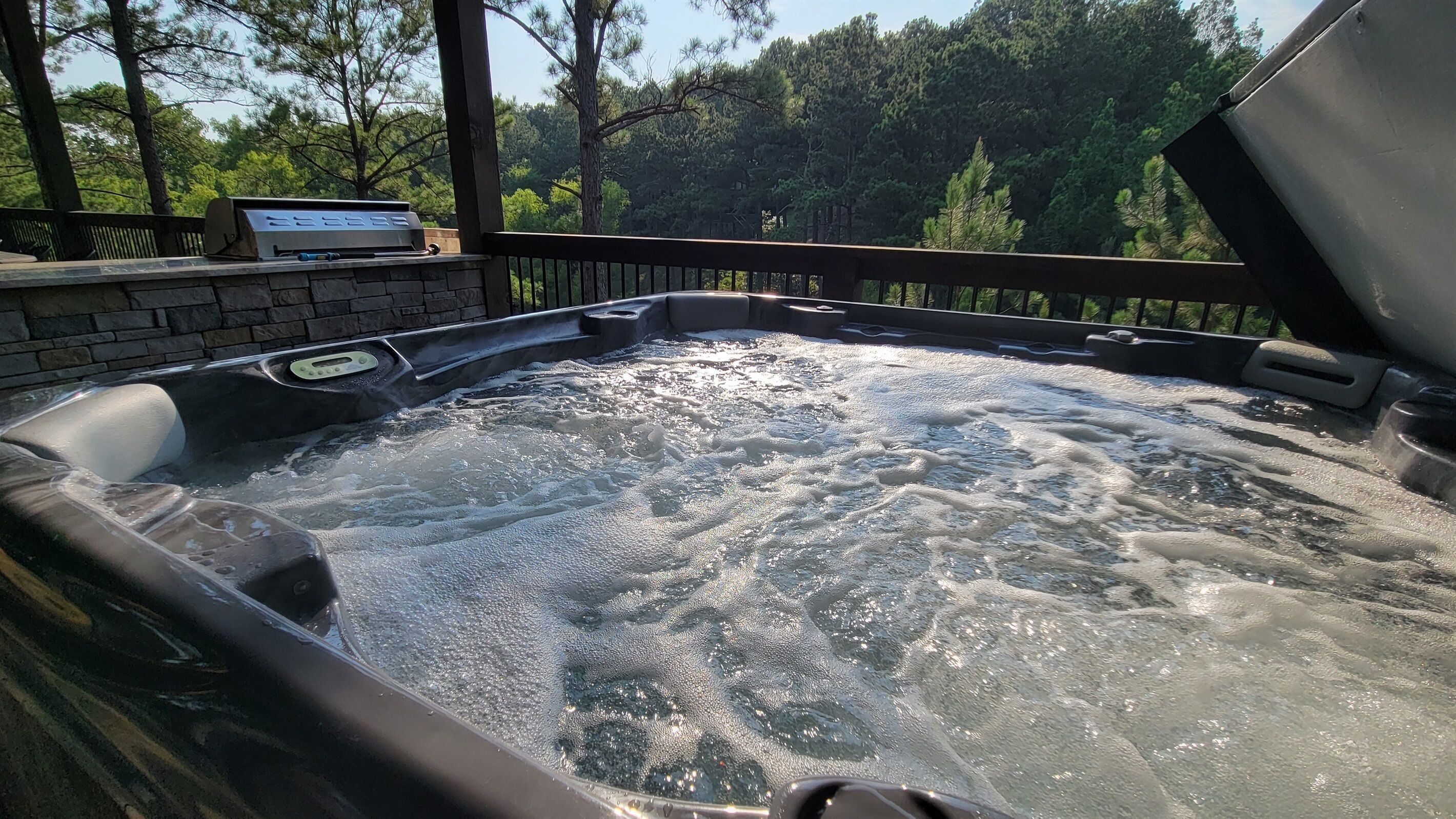 Un jacuzzi con cubierta de madera y pared de piedra, rodeado de árboles.