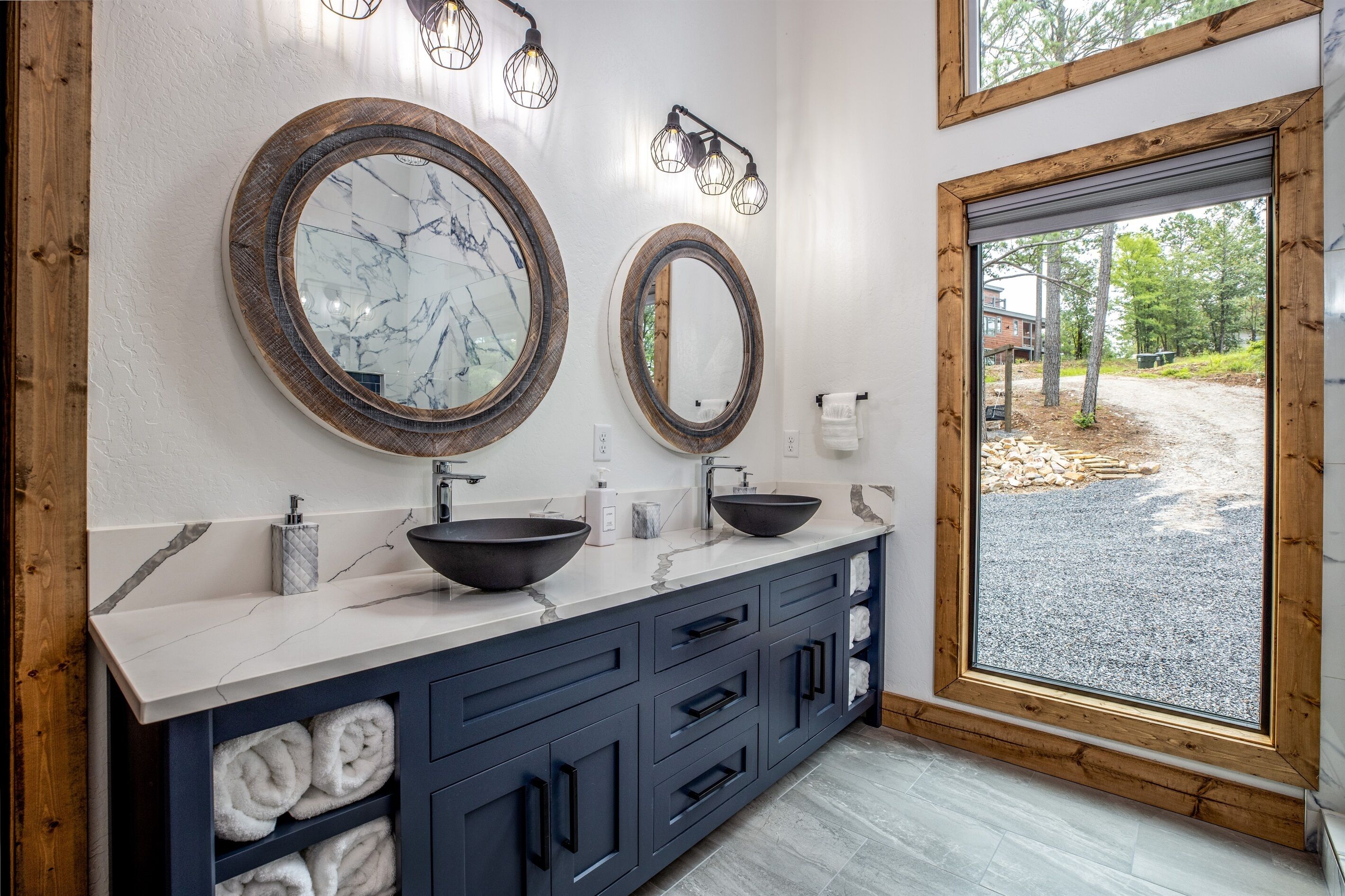 A bathroom with two large mirrors, a sink, and a window with a view of trees and a building.