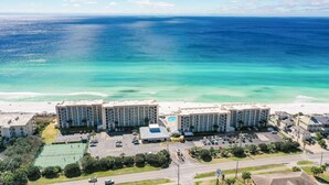A beachfront hotel with multiple buildings, a swimming pool, and a tennis court.