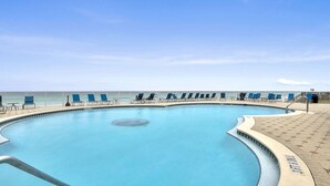 A pool with a curved edge, surrounded by blue lounge chairs, and a view of the ocean.