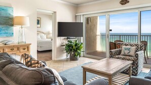 A spacious living room with a large window overlooking the ocean, a flat-screen TV mounted on the wall, and a cozy seating area with a coffee table.
