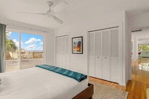 Un dormitorio con cama, ventilador de techo, balcón con sillas y vista al cielo.
