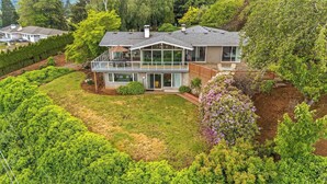 A modern two-story house with a large glass front, a covered patio, and a well-maintained garden.