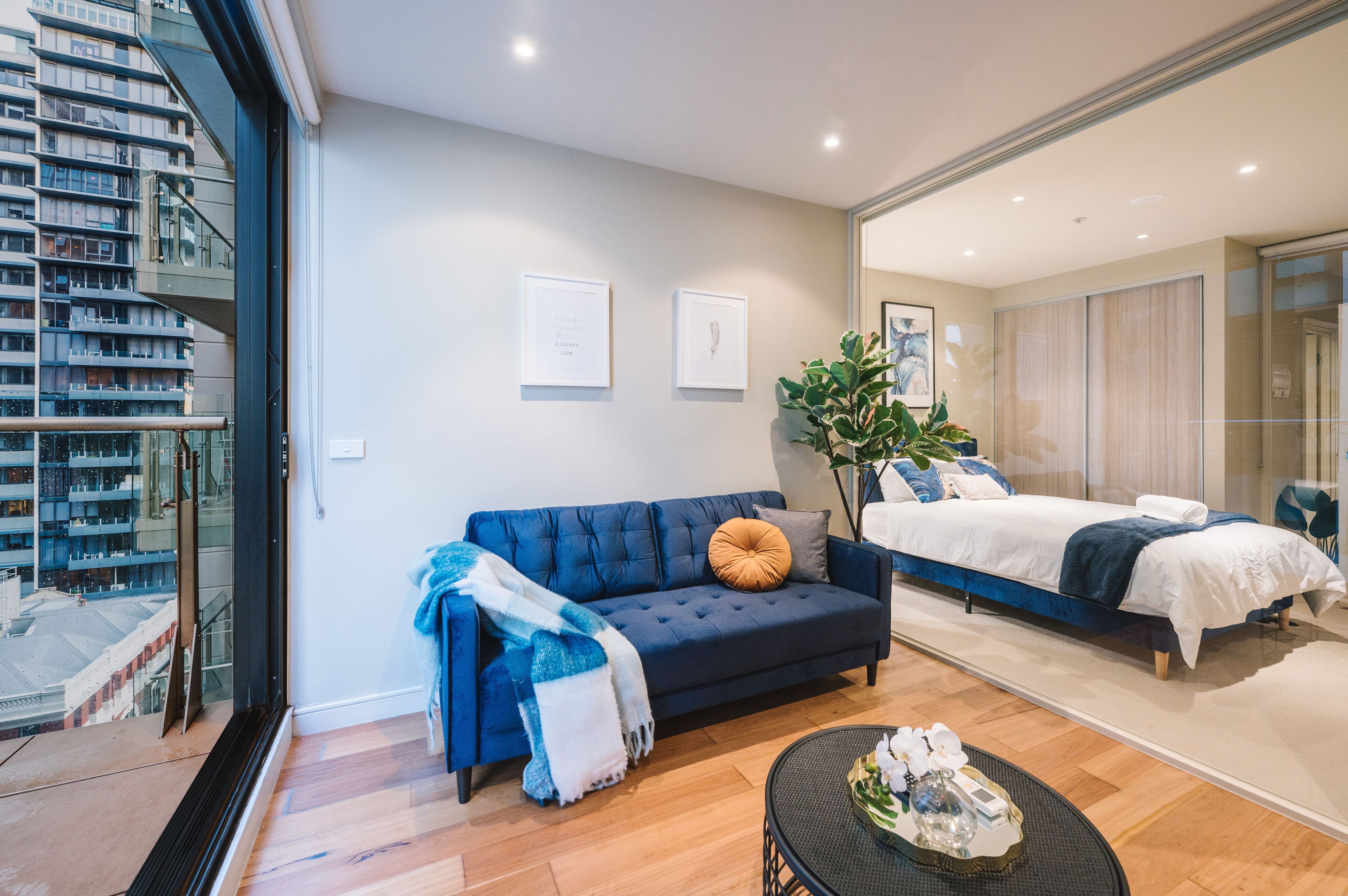 A modern hotel room with a large bed, a blue sofa, and a small table with decorative items.