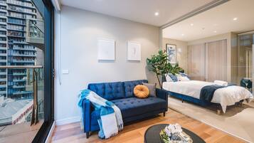 A modern hotel room with a large bed, a blue sofa, and a small table with decorative items.