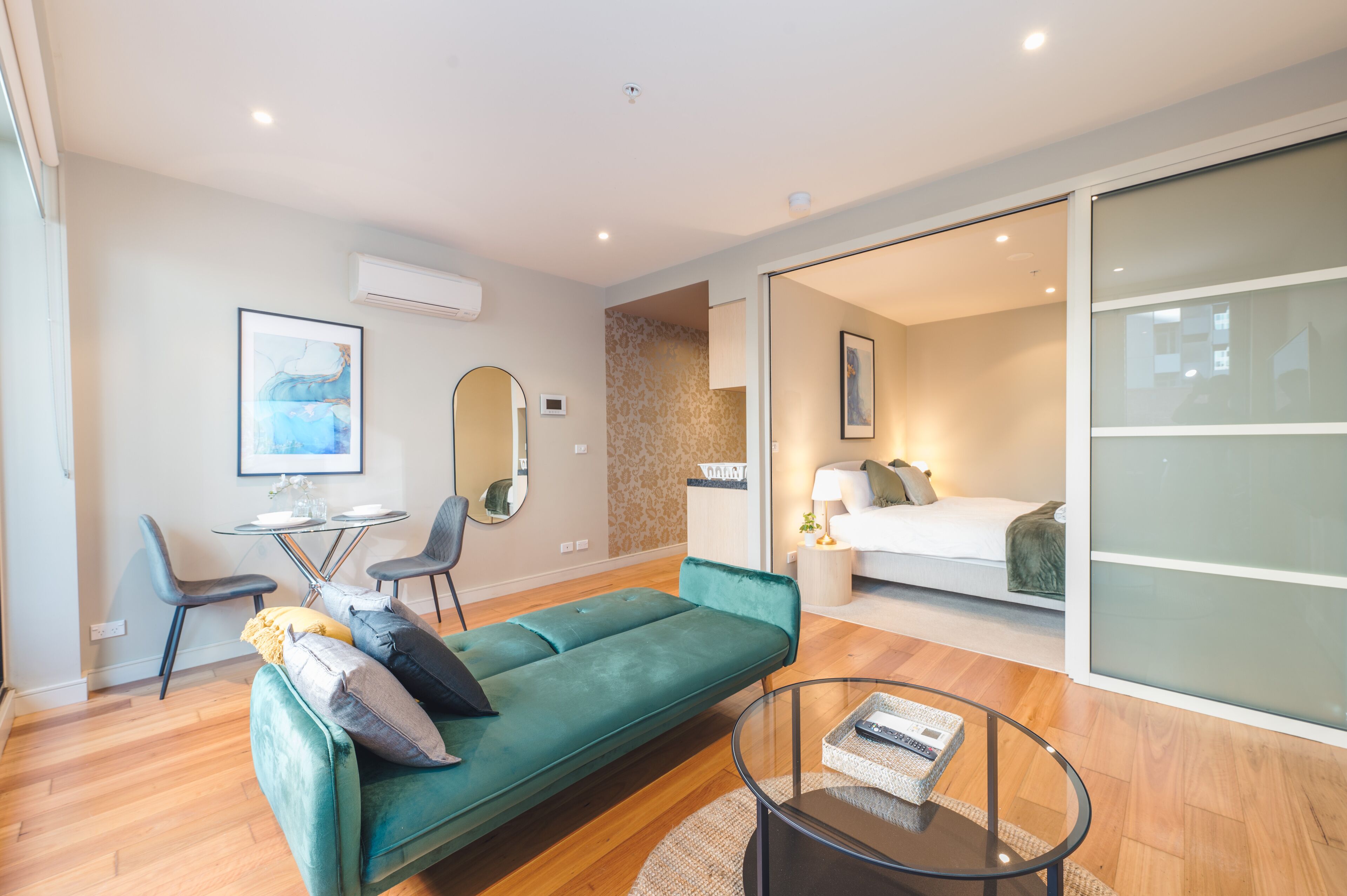 A modern living room with a green sofa, a round coffee table, and a dining area with chairs and a small table.