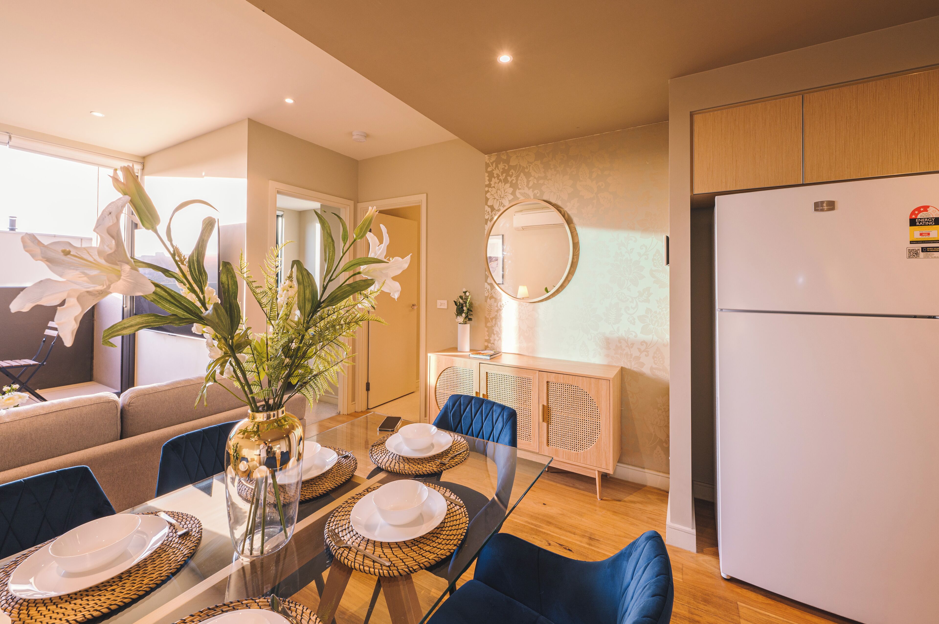 A modern dining area with a glass table, blue chairs, and a white refrigerator.