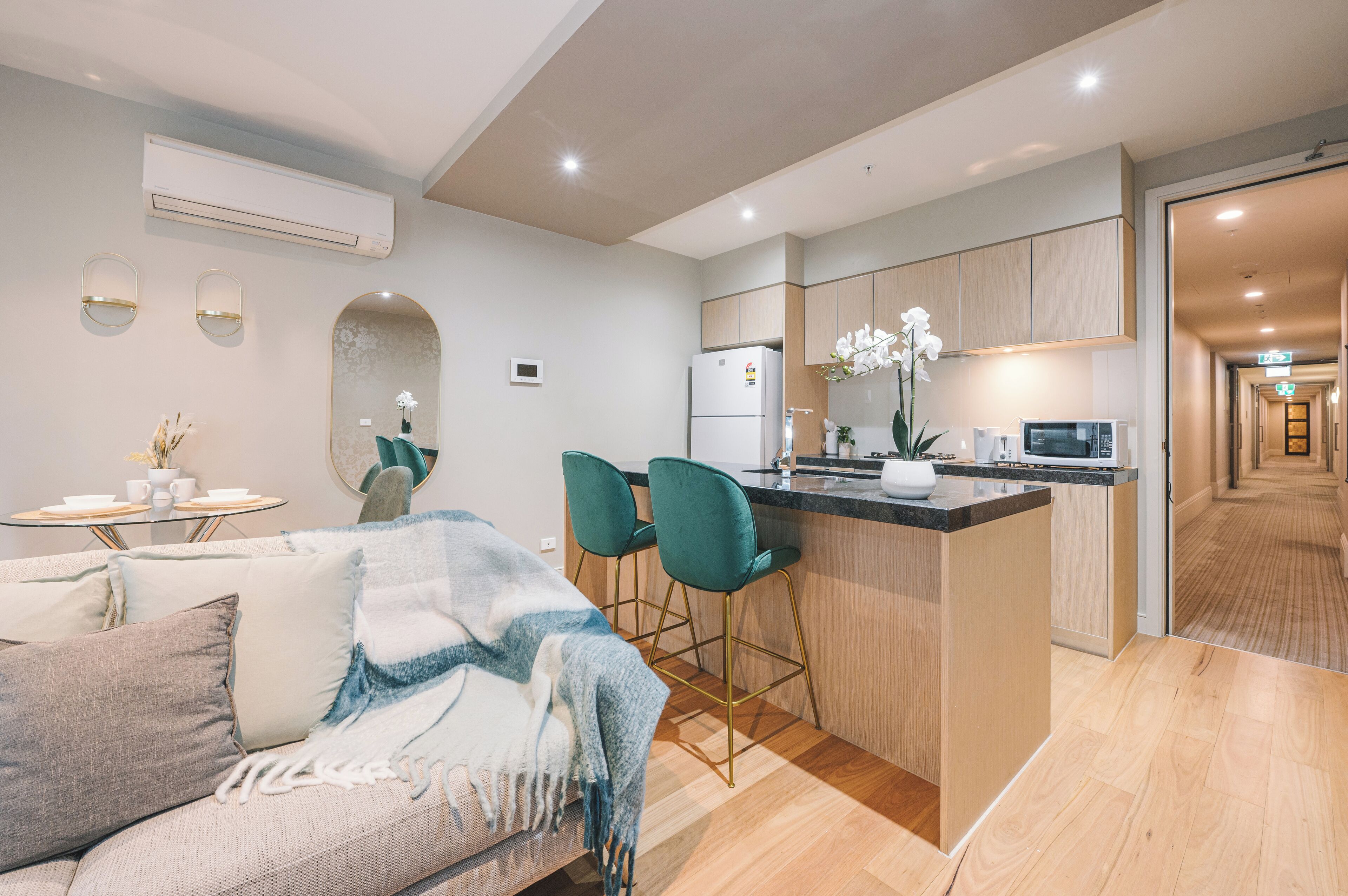 A modern apartment with a kitchen, dining area, and living room. It includes a sofa, two chairs, a small table, and a refrigerator.
