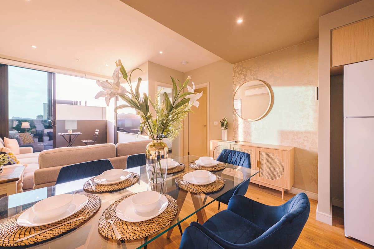 Un comedor moderno con una mesa de cristal, sillas azules y un jarrón con flores blancas.