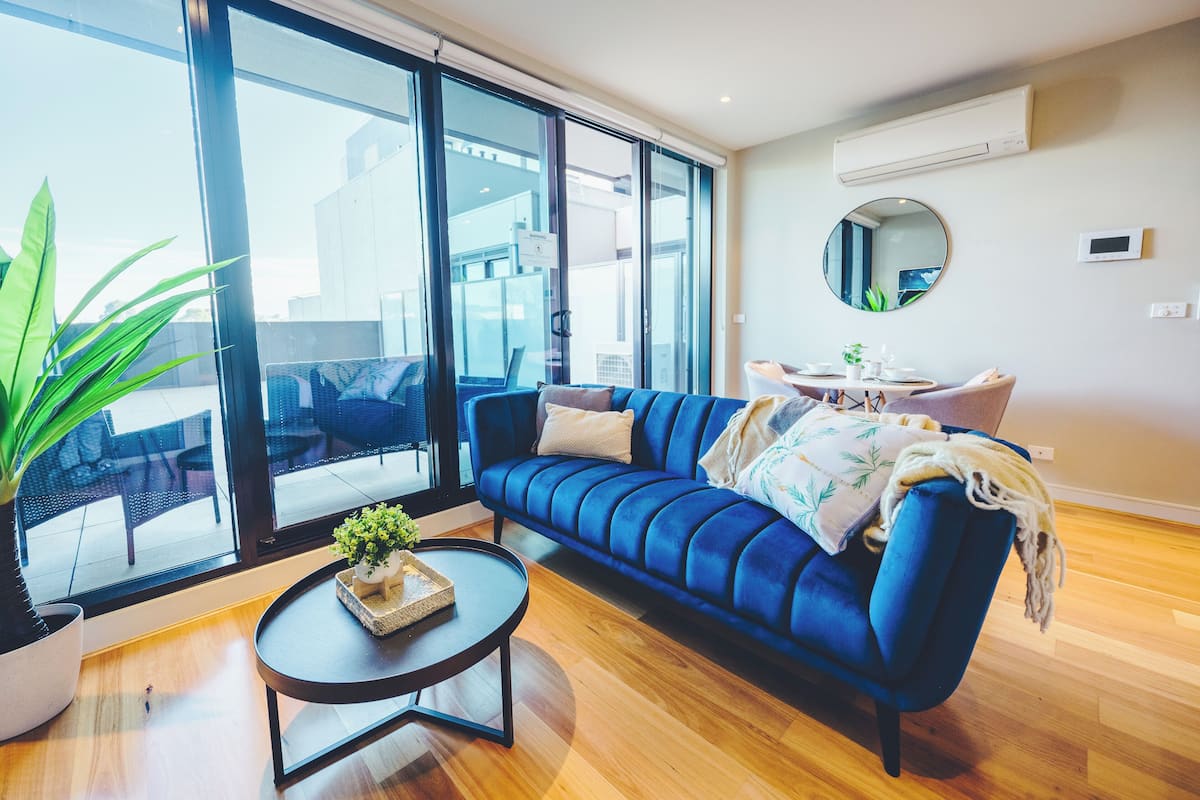 Un salón moderno con un sofá azul, una mesa de centro redonda y un ventanal con vistas a la ciudad.