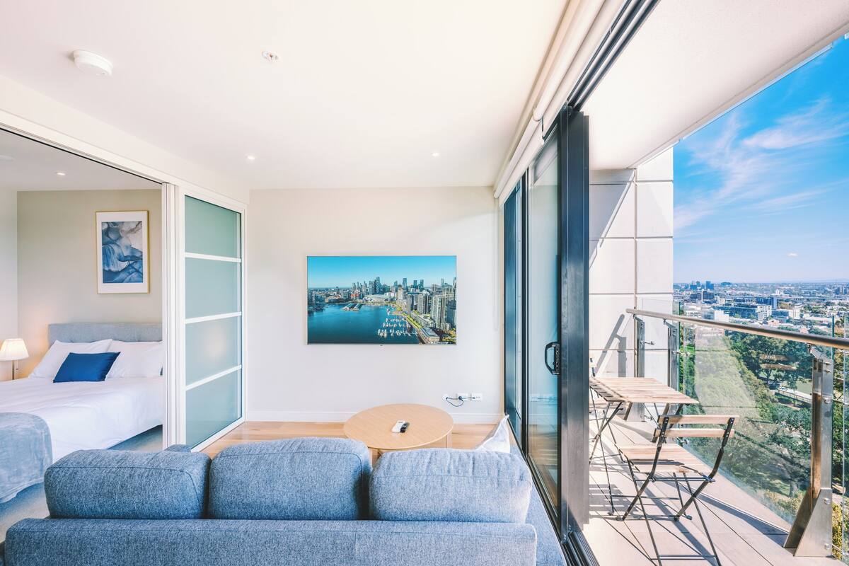 Una habitación de hotel moderna con una cama, un sofá, una mesita y un balcón con vistas a la ciudad.