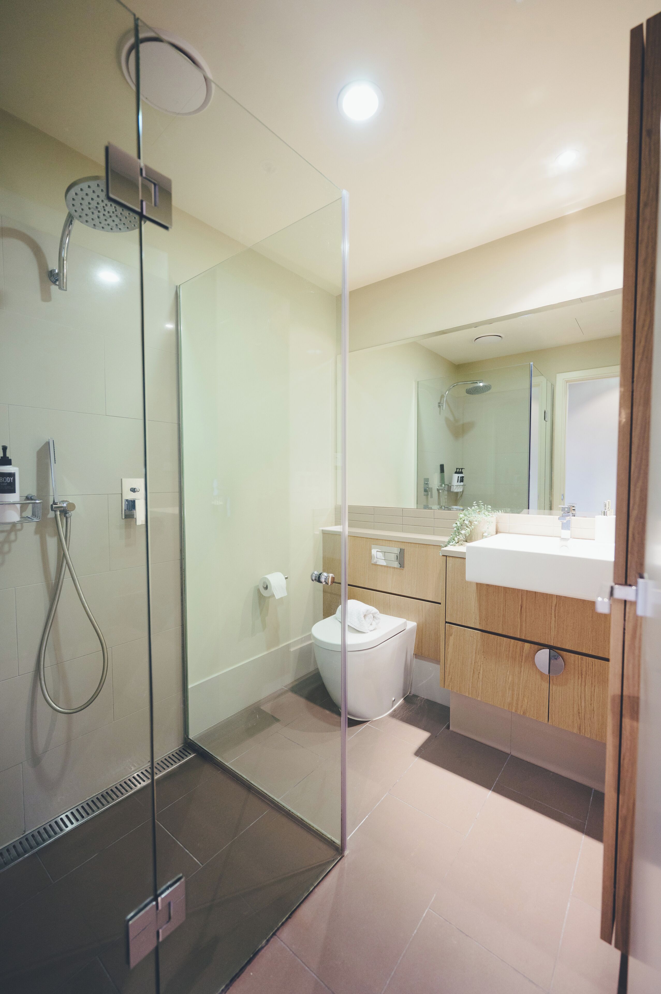 A modern bathroom with a glass shower enclosure, a toilet, a sink with a mirror, and wooden cabinetry.