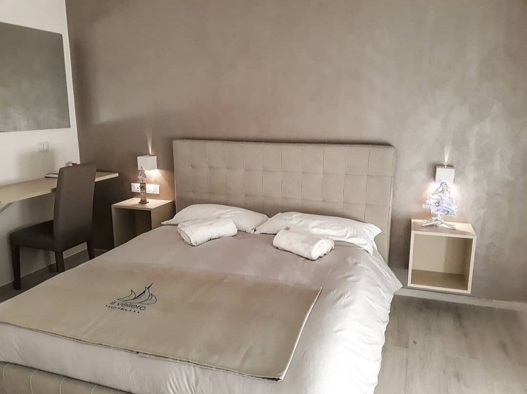 A neatly made bed with a headboard, two bedside tables with lamps, a chair, and a desk.