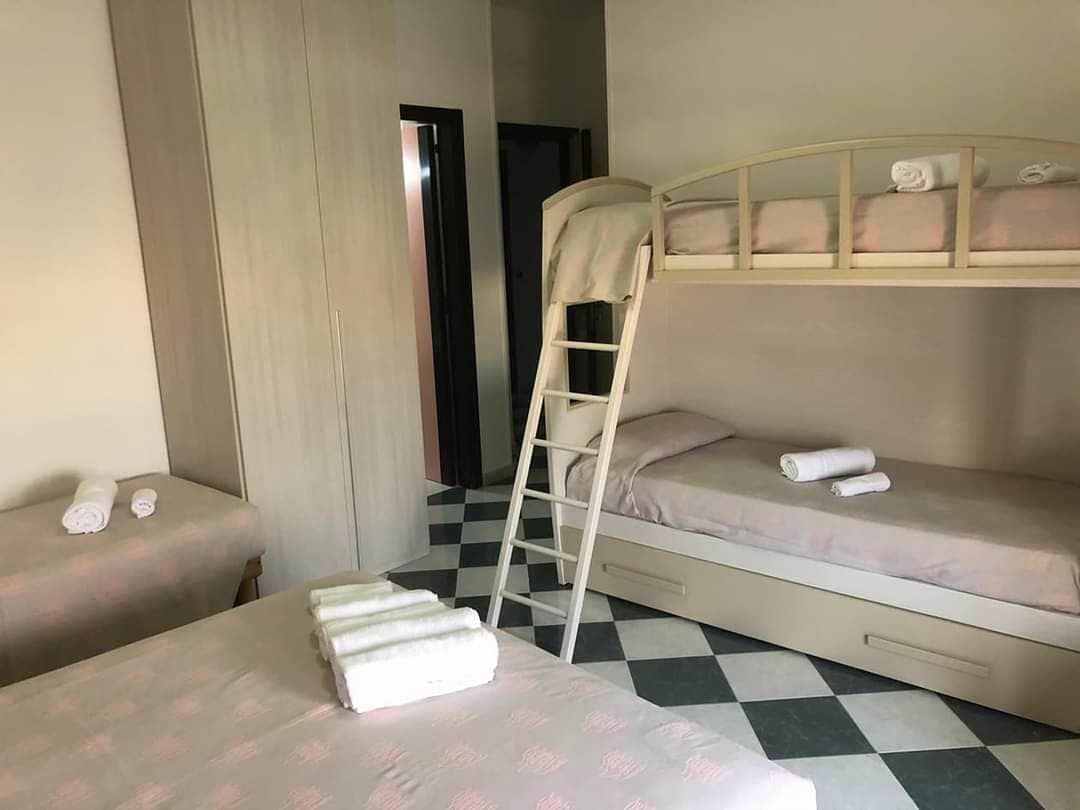Quarto com duas camas, uma beliche e outra de solteiro, ambas com toalhas bem dobradas.