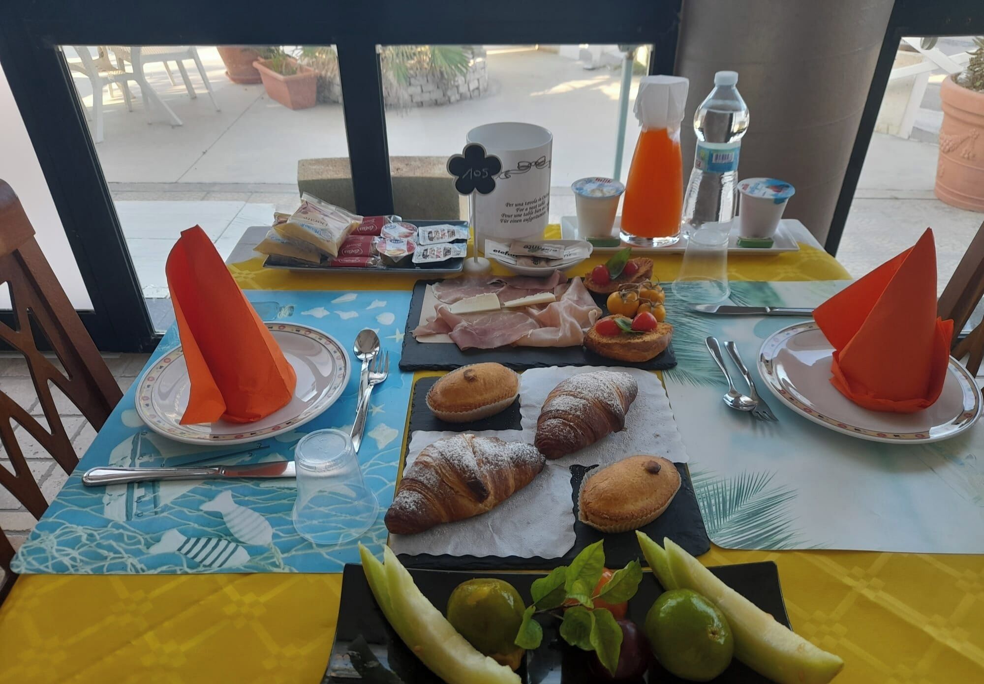 A breakfast table with croissants, fruits, and a water bottle.