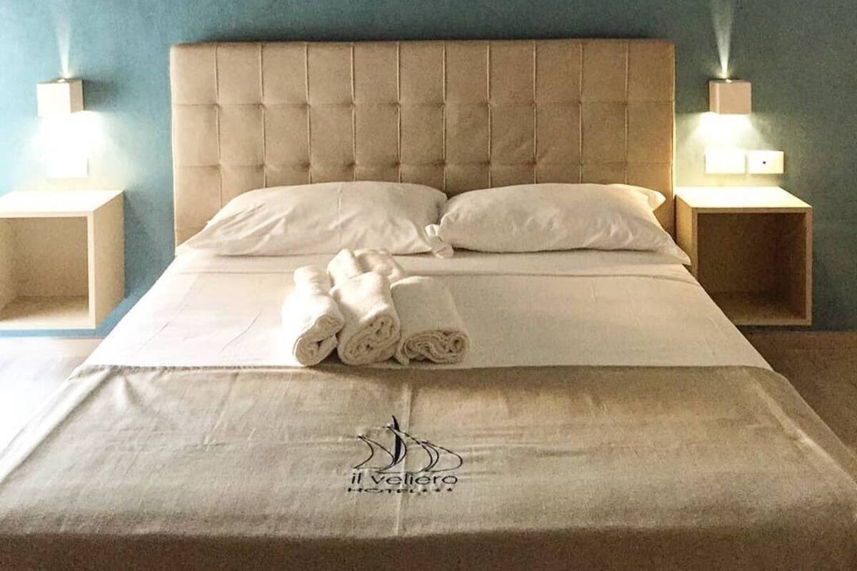 A neatly made bed with a tufted headboard, two bedside lamps, and rolled towels on the bed.