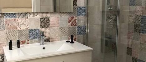 Um banheiro com pia branca, duas gavetas, espelho e box de vidro.