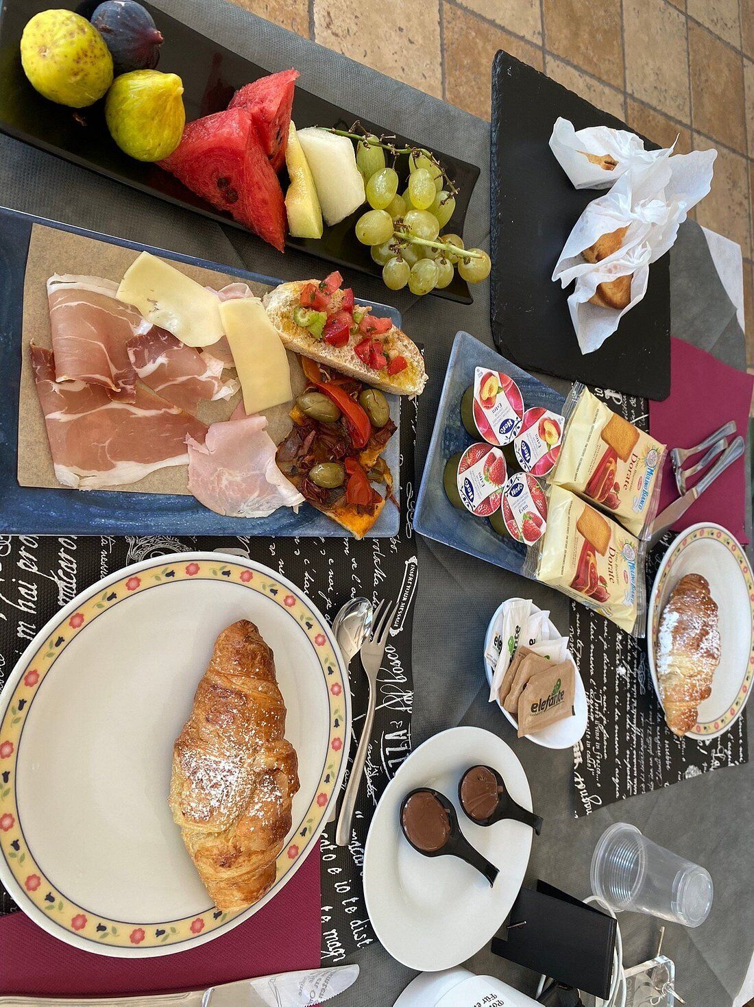 Una mesa con diversas opciones de comida, como frutas, quesos, embutidos y pasteles.