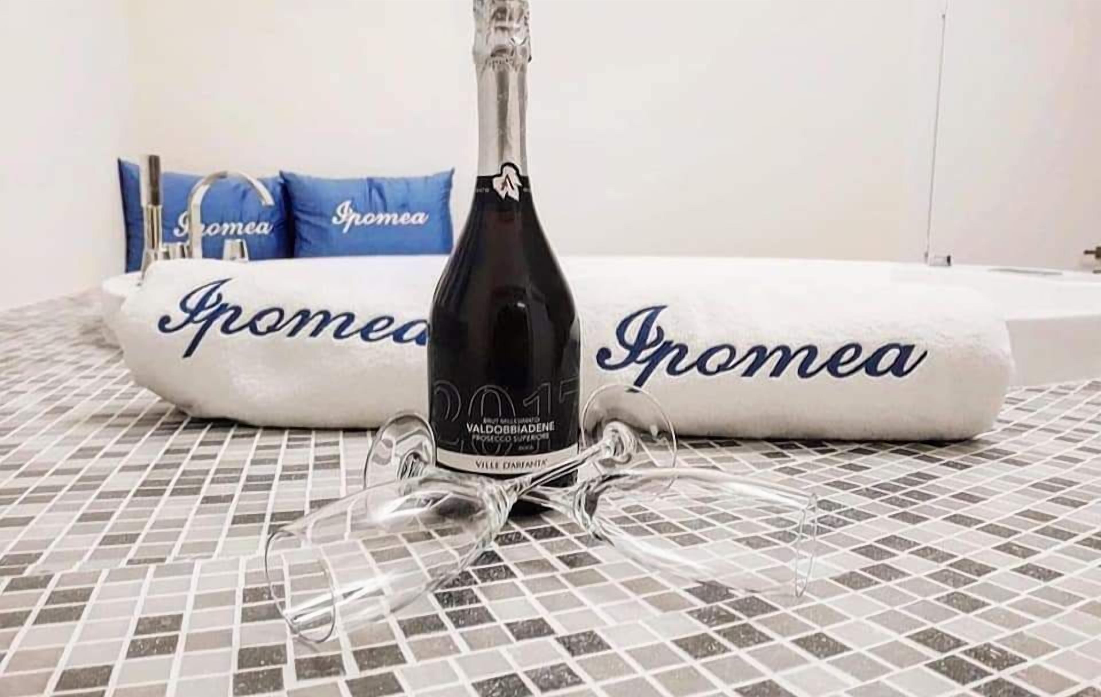 A bottle of wine on a tiled surface with a towel and pillows in the background.