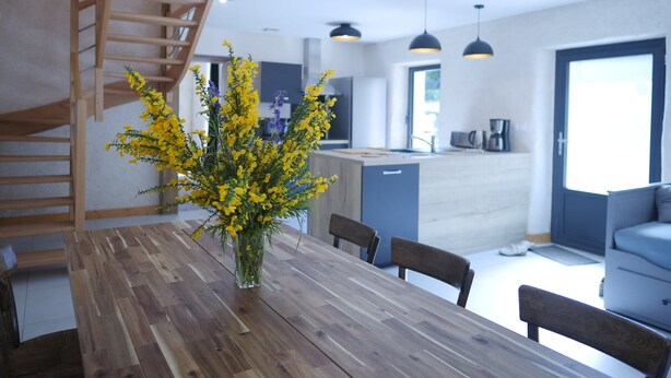 Une cuisine moderne avec une table et des chaises en bois, un vase rempli de fleurs jaunes et un escalier.