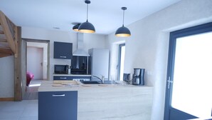 Une cuisine moderne dotée d’un îlot central, de luminaires suspendus noirs, d’un four à micro-ondes encastré et d’une machine à café.