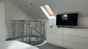 Un dormitorio moderno con tragaluz, televisor y escalera de metal.