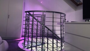 Un interior moderno con una escalera en espiral de metal, paredes blancas y un televisor de pantalla plana montado en la pared.