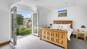 Un dormitorio con cama de madera, una mesita de noche, una lámpara y vistas a un paisaje verde a través de un ventanal grande.