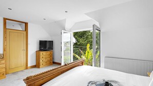 Un dormitorio con cama, cómoda de madera, televisor y balcón con plantas.