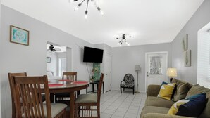 A dining area with a round table and chairs, a television mounted on the wall, and a ceiling fan.
