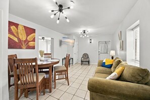 A living room with a dining area, a ceiling fan, and a TV mounted on the wall.