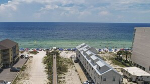 A beachside view with a clear sky, a sandy beach, and a row of buildings with balconies overlooking the ocean.