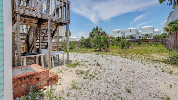 A beachfront property with a wooden deck, a brick wall, and a sandy area.