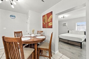 A compact room with a bed, a dining table with chairs, a wall clock, and a painting. - Cute cottage across from the Gulf (Gulf Shores)