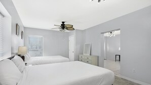 A bedroom with two beds, a ceiling fan, a dresser, a mirror, and a window with blinds.